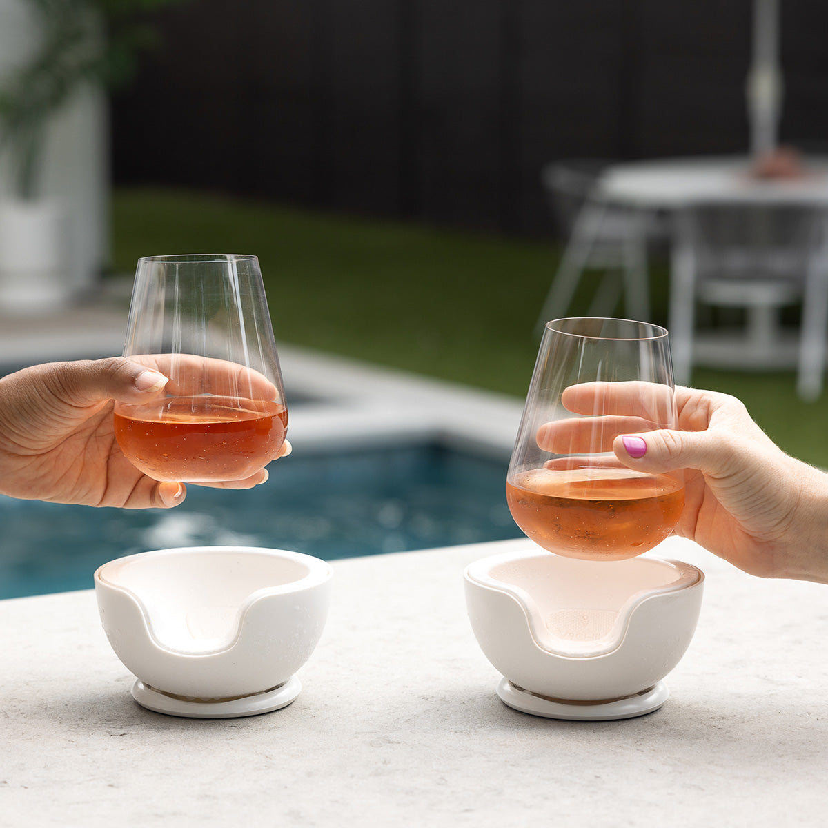 VoChill stemless wine chiller pair with hands placing stemless wine glasses with rosé wine in the chillers by the poolside