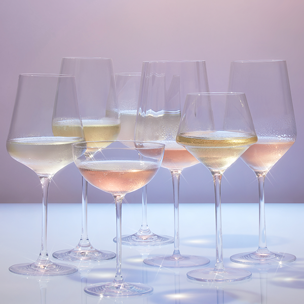Various sized stemmed wine glasses containing white wine and rose are against a light purple background. Condensation is on each perfectly chilled glass of wine.